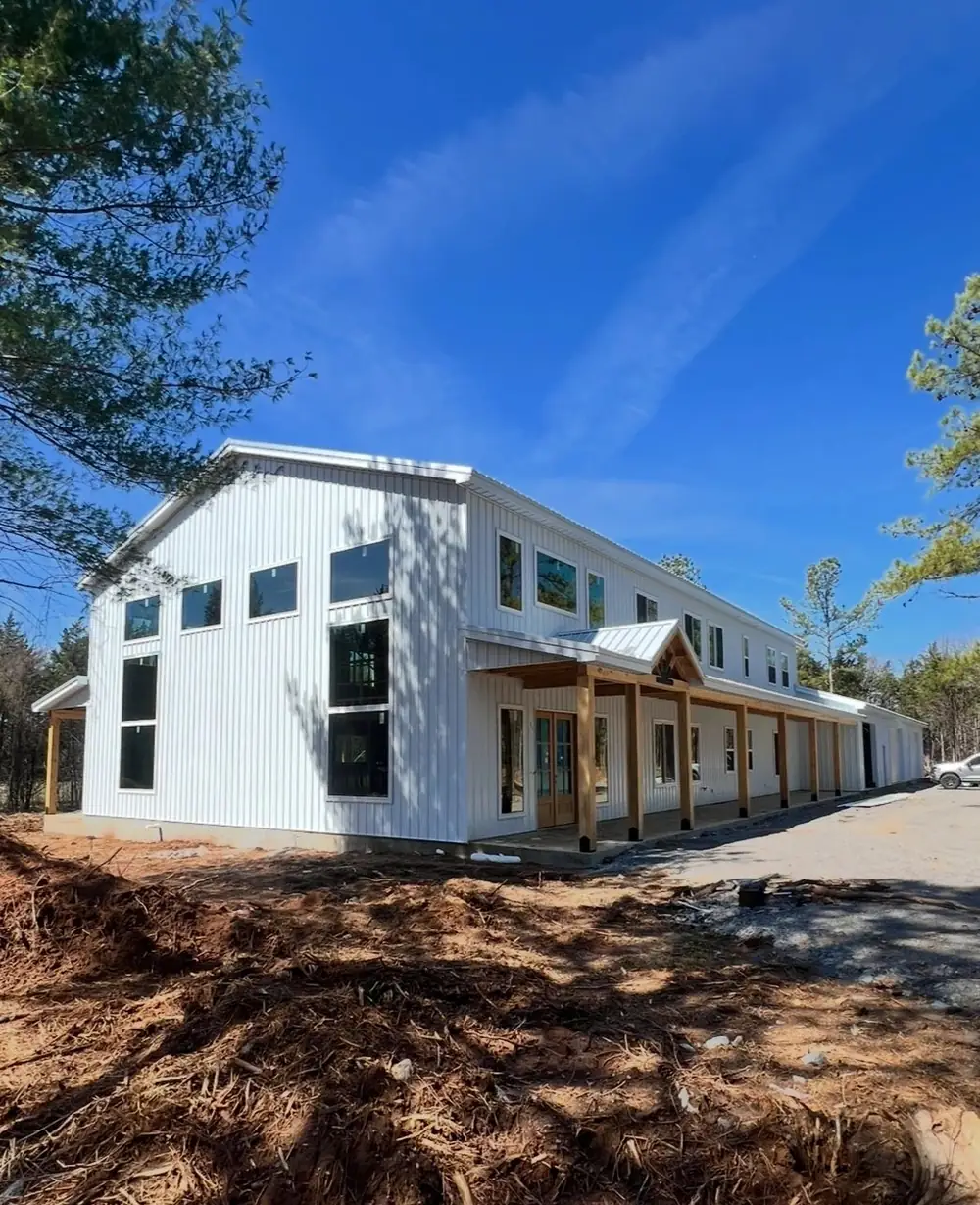 A finished two-story white board-and-batten barndominium with a long timber porch