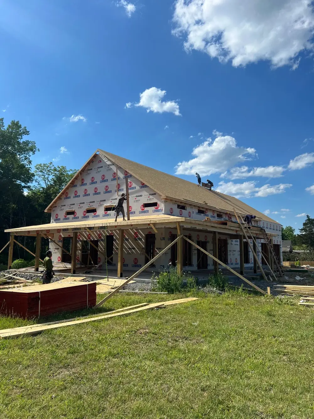 A large home framed and wrapped, with a metal roof going on and a timber porch across the front