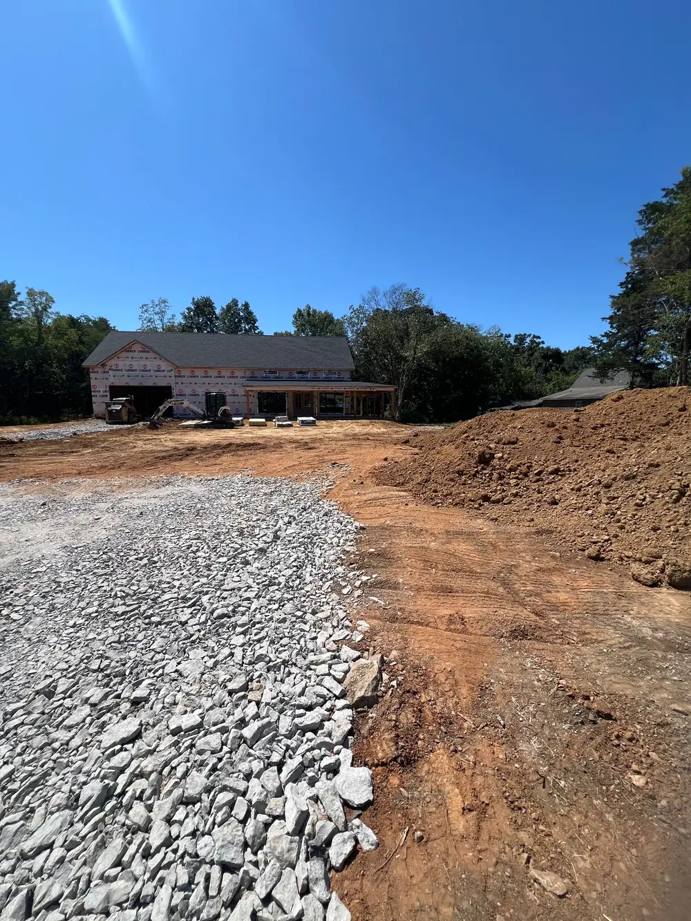Crushed stone drive and red clay fill on a building site with a new house behind