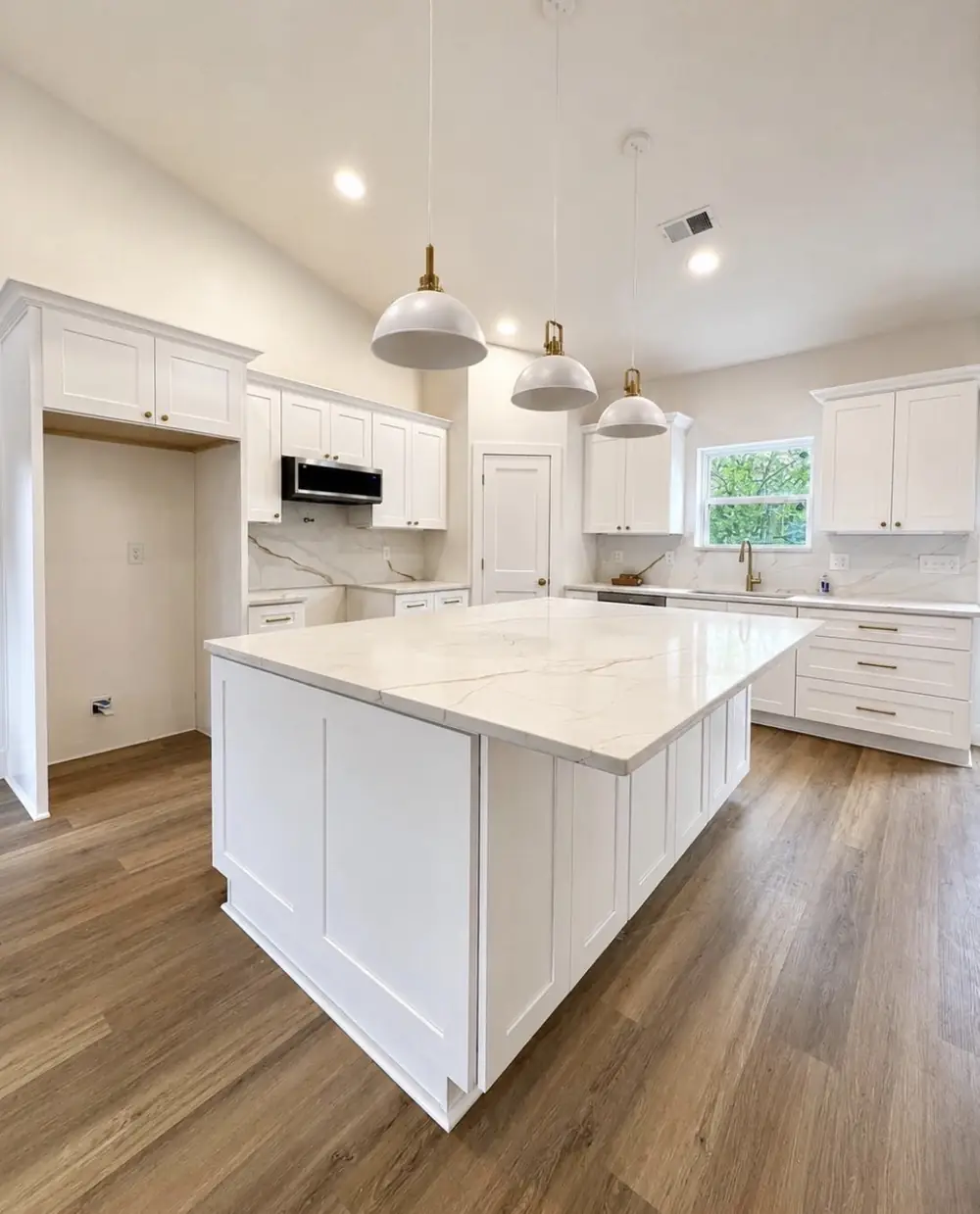 A finished kitchen with a large white island and pendant lights
