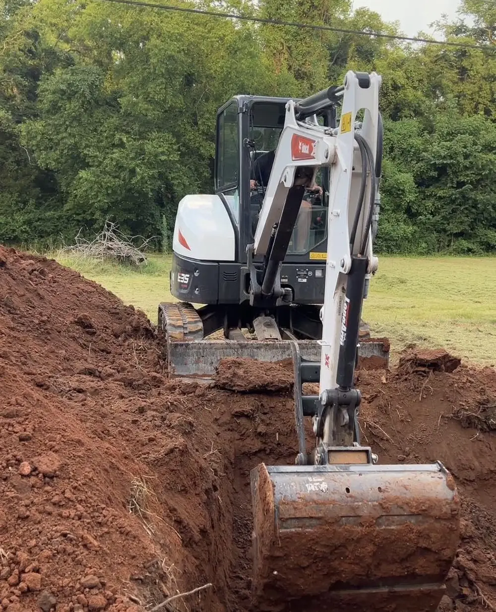 A mini excavator digging a trench through Middle Tennessee red clay